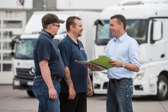 
Сотрудник транспортной компании беседует с двумя водителями грузовых транспортных средств